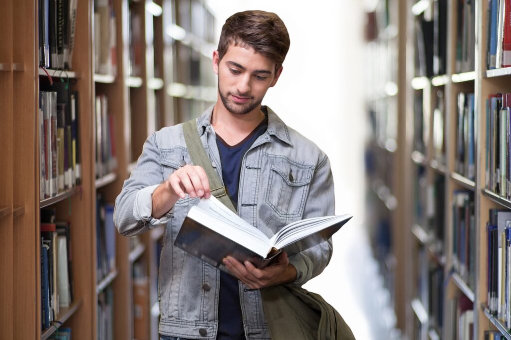 Estudiante revisando libros en la biblioteca para definir su tema de investigación.